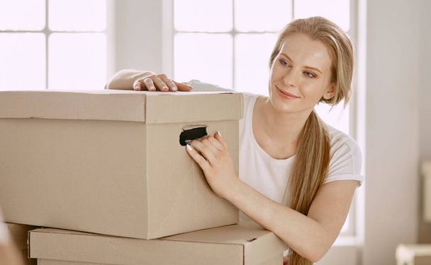 Een mooie alleenstaande jonge vrouw uitpakken dozen en verhuizen naar een nieuw huis - Foto, afbeelding