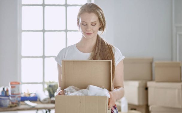 Kaunis yksittäinen nuori nainen purkamassa laatikoita ja muuttamassa uuteen kotiin - Valokuva, kuva