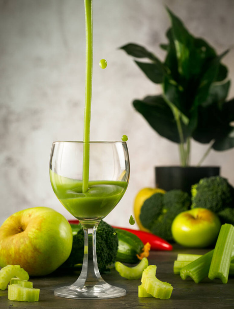 ガラスの中で絞りたての緑のジュースでまだ生活。ジュースはガラスに注ぎ、散布、セロリ、緑の野菜やリンゴが周りにあります。背景には怪物がいる. - 写真・画像