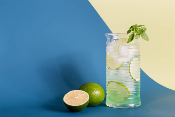Lime mojito with ice in glass at minimal blue and yellow background - Fotó, kép