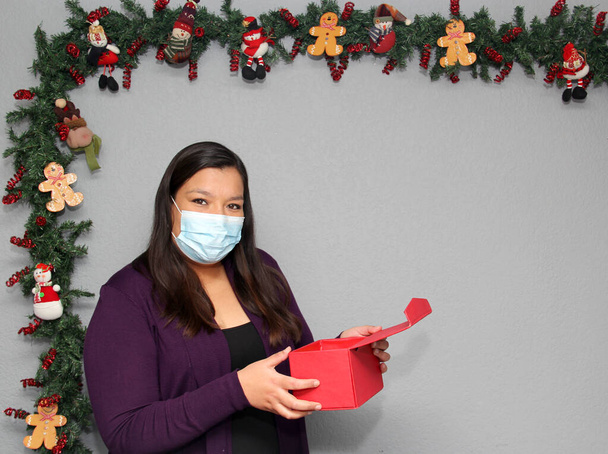 μαύρα μαλλιά Latin γυναίκα με μάσκα προστασίας και κουτί δώρου στη διακόσμηση των Χριστουγέννων, νέα κανονική covid-19 - Φωτογραφία, εικόνα