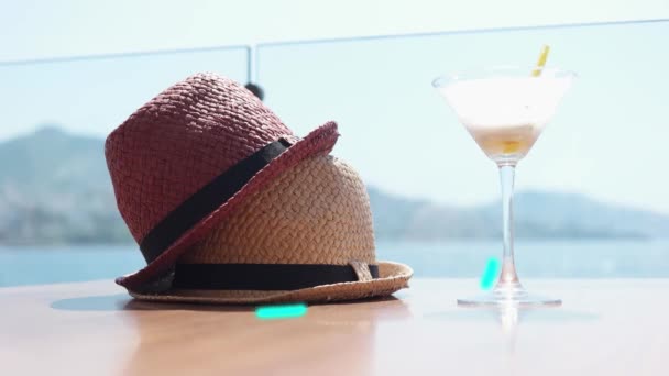 Efecto de línea brillante. Dos sombreros de paja y vasos de martini. Mesa de restaurante junto al mar y con vistas. Filmación que cuenta sobre vacaciones y viajes. - Metraje, vídeo