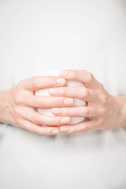 Beautiful female hands holding white cup. Manicure with natural color nail polish. Copy space, vertical - Photo, Image