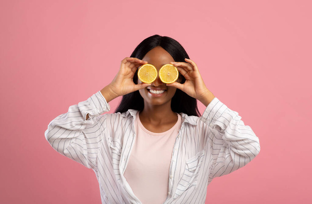 Happy young black lady with lemon halves in front of her eyes posing on pink studio background, panorama - Fotó, kép