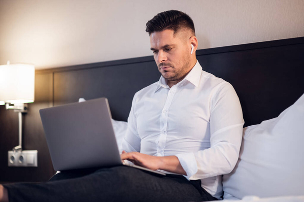 Молодий концентрований чоловік працює на своєму комп'ютері, сидячи на
 - Фото, зображення