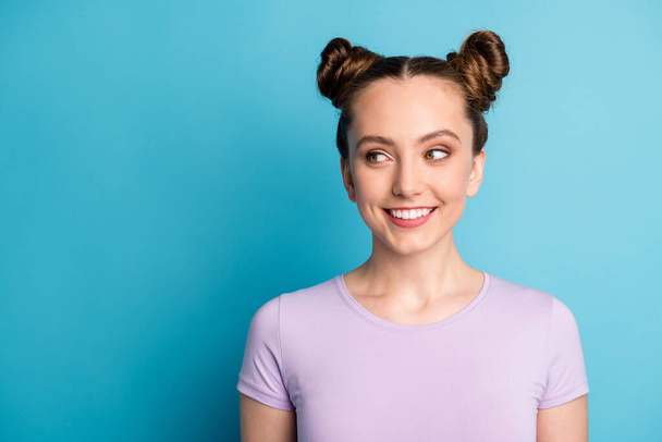 Closeup photo of attractive teen lady two funny buns good mood charming cute appearance look interested side empty space tricky wear casual purple t-shirt isolated blue color background - Foto, imagen