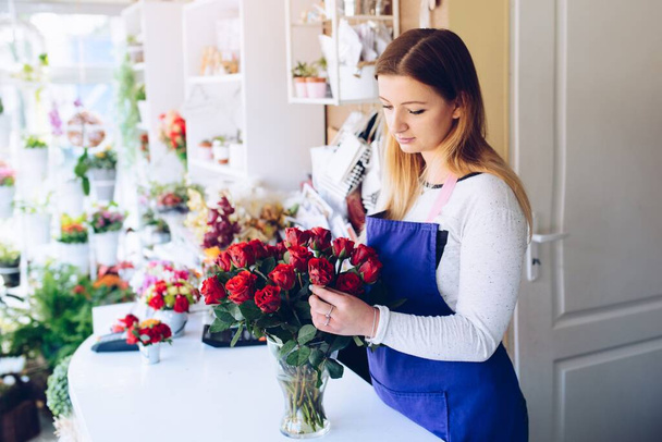 Mladá žena květinářství v květinářství dává růže do vázy. - Fotografie, Obrázek