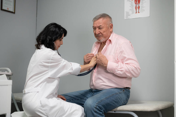Ein Arzt überprüft den Gesundheitszustand ihrer älteren Patientin mit einem Stethoskop. Epidemiekonzept verhindern - Foto, Bild
