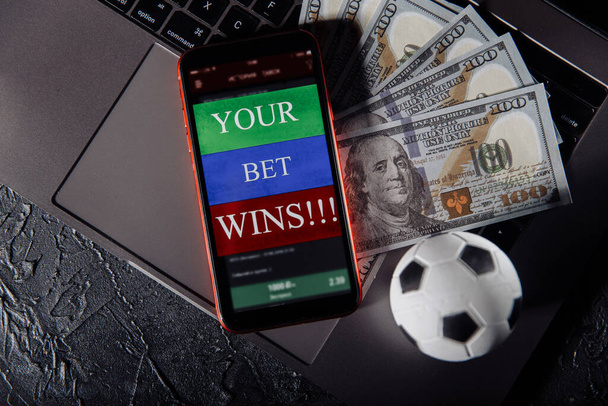 Smartphone met gokken mobiele applicatie, bal en geld bankbiljetten op een toetsenbord close-up. Sport en weddenschappen - Foto, afbeelding