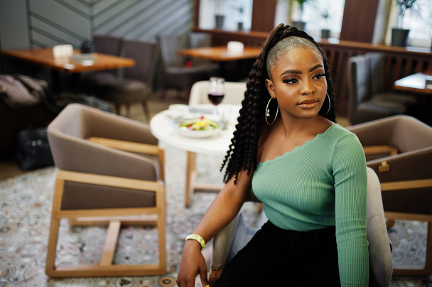 Portrait of attractive young african american woman wearing in green sweater and black jeans pose at restaurant. - Фото, зображення