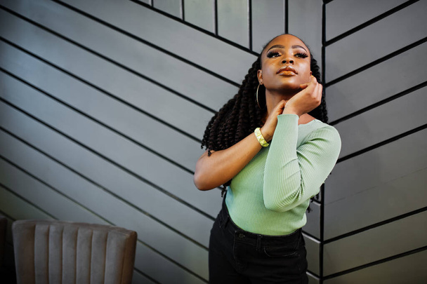Muotokuva houkutteleva nuori afrikkalainen amerikkalainen nainen yllään vihreä pusero poseeraa harmaa seinä. - Valokuva, kuva