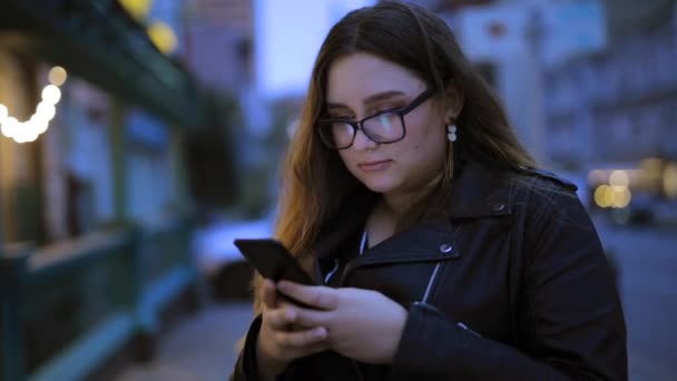 vrouw is chatten in de smartphone tegen de achtergrond van de avond stad - Video