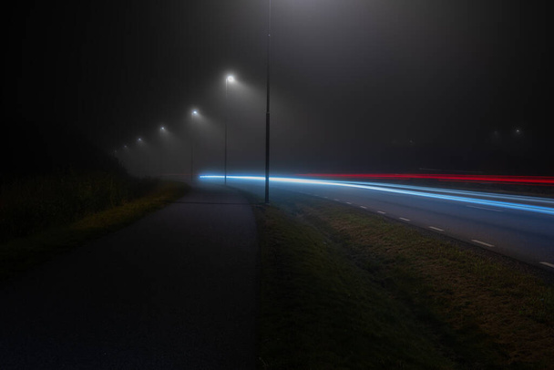 Yoğun siste gece vakti ıssız bir yolda uzun süre araba ışıkları yanar... - Fotoğraf, Görsel