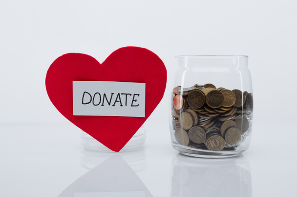 Red heart with DONATE word and coins in glass jar. Charity and donation concept - Photo, Image