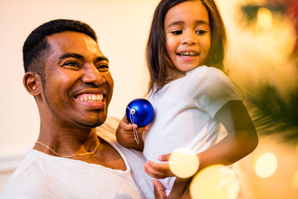 happy mixed race father and cheerful beautiful daughter decorating interior in livingroom - Photo, image
