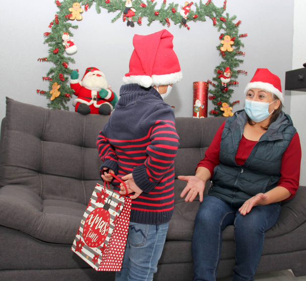grand-mère et enfant avec masque de protection et santa claus chapeau, cadeaux et décorations de Noël, nouveau normal covid-19 - Photo, image