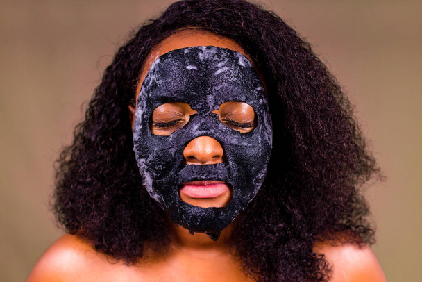 Young woman with bubble sheet mask on her face on brown background - Foto, afbeelding