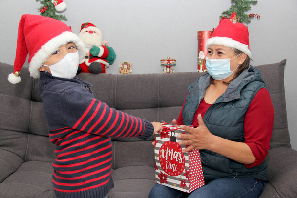 Grootmoeder en kind met beschermkapje en kerstmuts, cadeaus en kerstversiering, nieuwe normale covid-19 - Foto, afbeelding