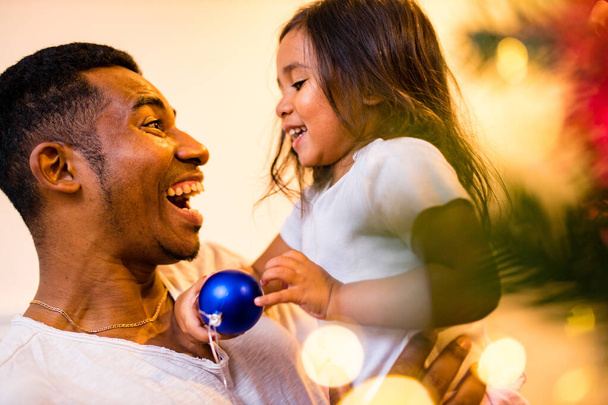 happy mixed race father and cheerful beautiful daughter decorating interior in livingroom - Photo, image