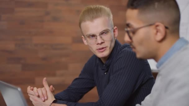 Medium close up of smart caucasian man discussing business plan with his middle eastern partner sitting together indoors in modern office - Footage, Video