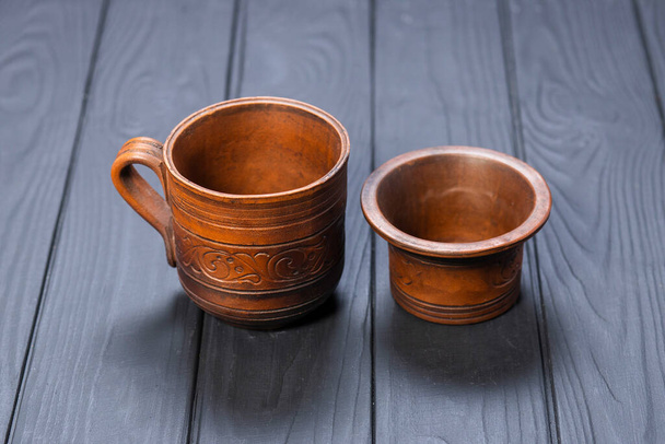 hliněný pohár a malá miska na černém dřevěném pozadí - Fotografie, Obrázek