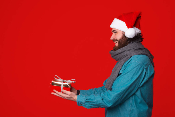 Merry man wearing a Christmas hat is giving a wrapped gift over. - Photo, Image
