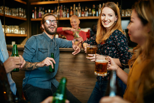Πολυπολιτισμική ομάδα καλύτερων φίλων που κάθονται σε μια παμπ, κουβεντιάζοντας και πίνοντας μπύρα. - Φωτογραφία, εικόνα