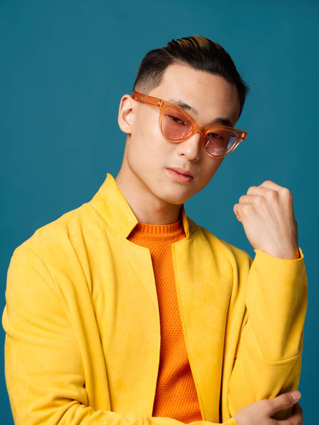 trendy man met oranje bril op een blauwe achtergrond en een geel jasje - Foto, afbeelding