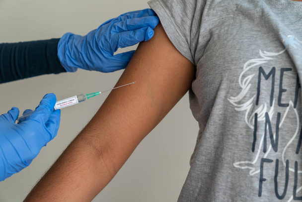 Kék latex kesztyűt viselő női orvos, aki egy gyermeket injekciózott a karjába egy tűvel és fecskendővel, amely a COVID-19 vakcina ellenszerének egy adagját tartalmazza immunizálással - 022 - Fotó, kép
