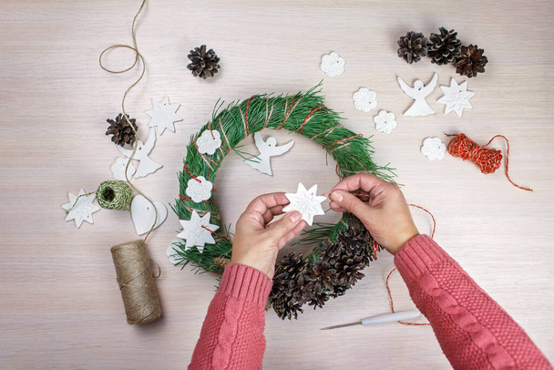 Woman making a fir wreath for Christmas Eve and decorating it with stars and angels with homemade salt dough, diy craft decoration, winter traditions, seasonal holidays. Top view - Photo, Image