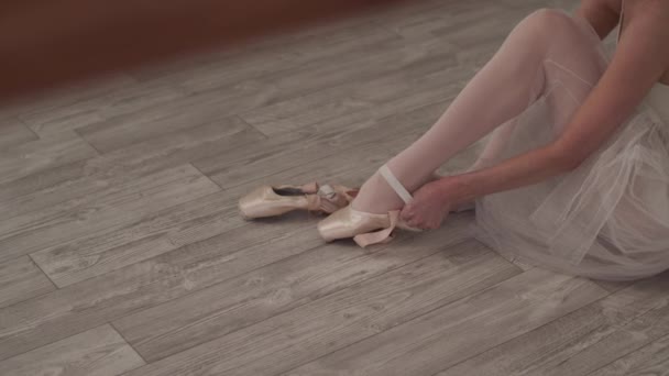 La ballerina si siede sul pavimento, indossa scarpe da punta e lega i nastri intorno ai piedi. - Filmati, video