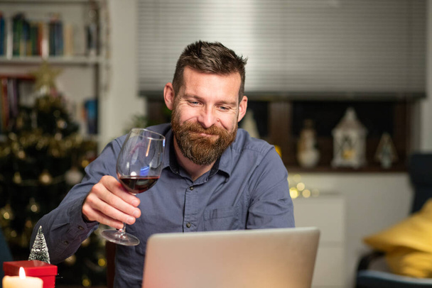 Porträt eines gutaussehenden Mannes, der Heiligabend zu Hause mit Laptop verbringt - Foto, Bild
