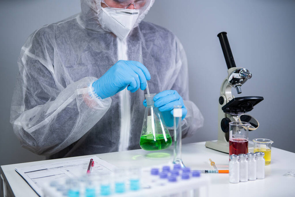 研究者は、エルレンマイヤーフラスコ混合物中の緑の生化学製品を振ると実験室での研究。コロナウイルスパンデミック研究所COVID 19研究室助手。医薬品開発医学研究. - 写真・画像