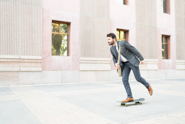 Businessman in his 30s with a suit skating to his work building. Latin man using an alternative transport to commute to his work - Fotografie, Obrázek