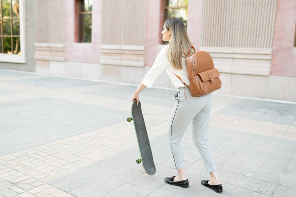 Blond female worker in her 30s preparing to ride a skateboard to travel to her job in the city  - Photo, Image