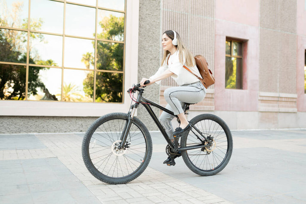 Vista lateral de una mujer de negocios utilizando un vehículo alternativo para llegar a su oficina de la ciudad. Mujer montando una bicicleta ecológica  - Foto, Imagen