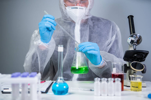 A tudósok zöld folyadékot ráznak a főzőpohárban. Fiatal laboratóriumi asszisztens, aki teszteket vagy kutatásokat végez a laborban. Technikus tesztelés kémia laboratóriumi kísérlet és rázás üveg cső lombik együtt mikroszkóp. - Fotó, kép