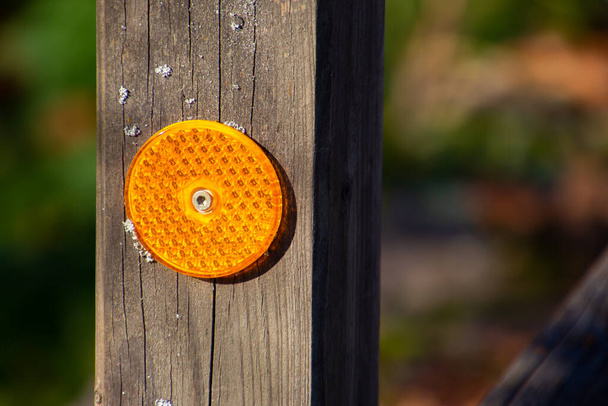 Reflector redondo de plástico naranja brillante en un poste de madera - Foto, imagen
