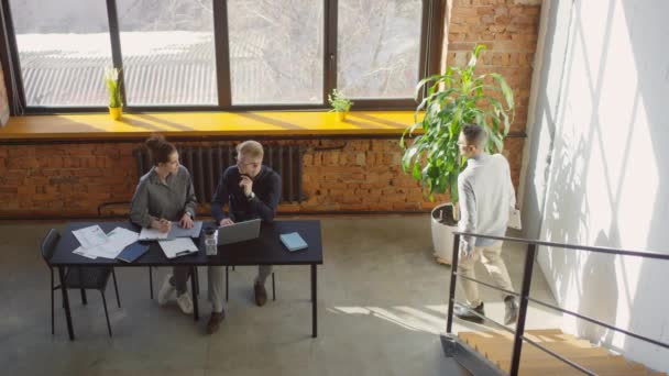 Κορυφαία προβολή βίντεο νέων ειδικών που εργάζονται σε φορητό υπολογιστή στο γραφείο από μεγάλο παράθυρο στη σοφίτα του γραφείου και τον επόπτη βοηθώντας τους, ενώ πηγαίνει από - Πλάνα, βίντεο