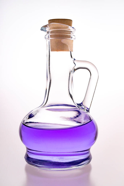 Glass container with blue liquid. A mysterious substance in a glass vial closed with a stopper. Light background. - Foto, Imagem