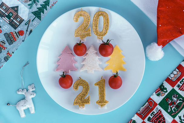 Xmas, kış, yeni yıl konsepti - Kırmızı altın ve beyaz ağaç oyuncaklarıyla mavi Noel arkaplanı, Noel Baba şapkası, 2021 numara mumlar ve hediye edilmiş oyuncak bisiklet. Düz, üstten, yukarıdan. Boşluğu kopyala - Fotoğraf, Görsel