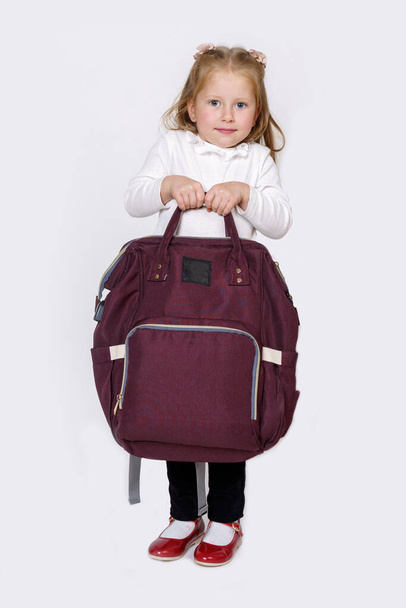 Children concept. The girl holds in her hands a large backpack bag. Isolated over white background. - Photo, Image