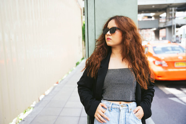 Portret młodej Azjatki w okularach przeciwsłonecznych i czarnej kurtce na ulicy. - Zdjęcie, obraz
