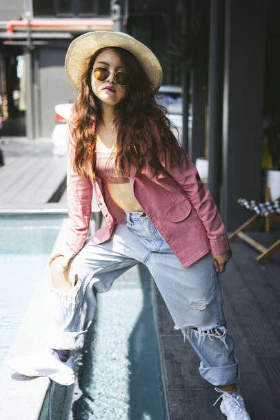 Fashion portrait of young asian woman wearing sunglasses, pink jacket, and hat on street. - Fotografie, Obrázek