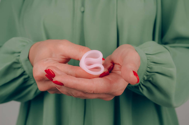 Close up of woman hand with perfect manicure, holding pink menstrual cup - demonstration of how to use, c form. Women health and hygiene concept, alternative hygiene products - Photo, Image
