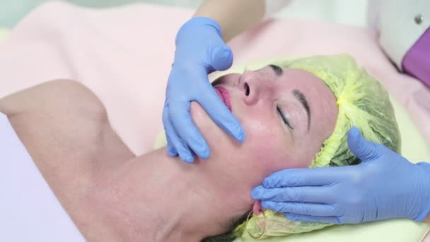 Close up portrait of charming woman with closed eyes enjoying skincare procedure. Masseuse arms touching client chin and nose. Anti-aging effect - Footage, Video