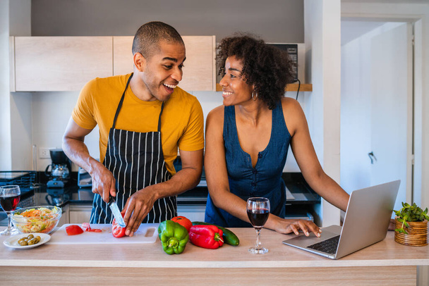 Latin couple using laptop while cooking in kitchen. - 写真・画像