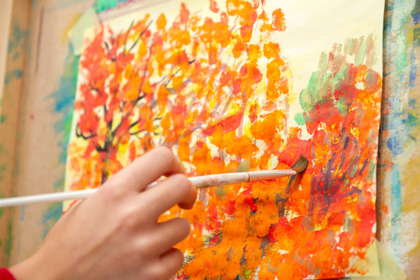 Young artist paints orange autumn trees on canvas - Фото, изображение