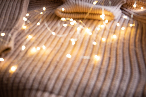 Світло світлої гірлянди на в'язаному светрі на столі. Фон з м'яким фокусом. Новорічна концепція
. - Фото, зображення