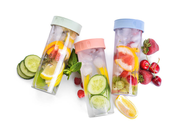 Flessen van muntwater met bessen en citrusvruchten op witte achtergrond - Foto, afbeelding